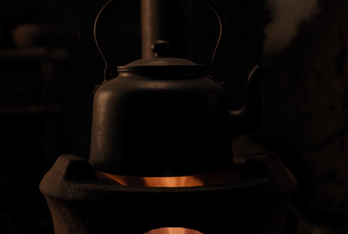 An iron kettle warming over a glowing clay stove